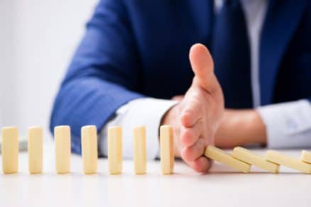 Businessman stopping dominoes, highlighting idea of pinch points.