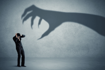 Fearful businessman alongside scary hand shadow.